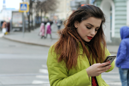 Girl is talking on the phone while walking around the city. She has long brown hair and is dressed in a light green jacketの写真素材
