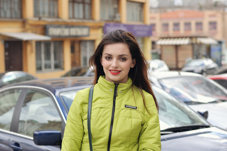 Portrait of a stylish girl who walks around the city and the wind blows her long brown hair. She is dressed in a green jacket and has a good mood.の写真素材