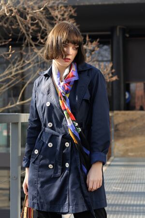 ?eautiful girl is walking in the park. She has brown hair and a bob hairstyle, she is wearing a blue raincoat and a scarf around her neck.の写真素材
