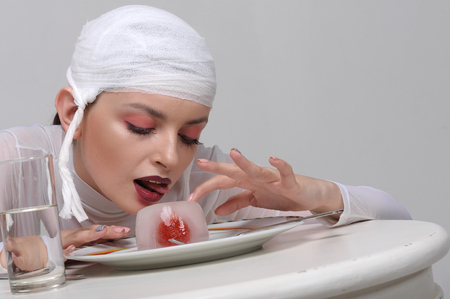 Fashion portrait of a sick girl with a bandage on her head who eats artificial foodの写真素材