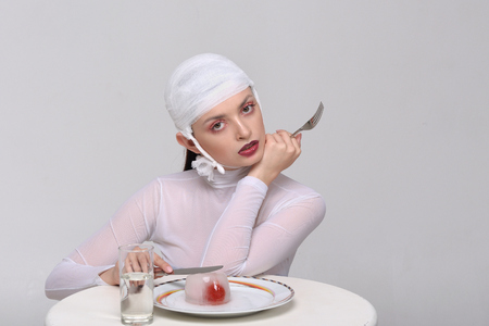 Fashion portrait of a sick girl with a bandage on her head who eats artificial foodの写真素材
