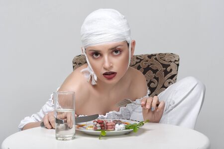 Fashion portrait of a girl with a bandage on her head who sits at the table and has a lunch of medicinesの写真素材