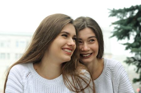 Two girlfriends are laughing fun. They both have long brown hair that is long to the waist and they are dressed in identical white sweaters.の写真素材