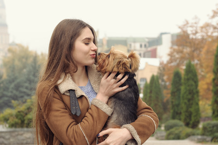 Girl holds a small dog in her arms, hugs and kisses her, warming her from the autumn cold.の写真素材