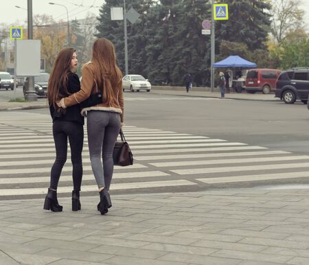 Two girls trying to cross the road at a pedestrian crossing. They have long brown hair and slender...
