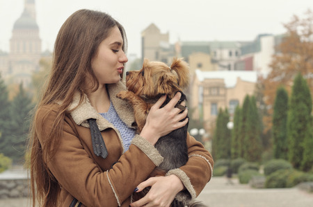 Girl holds a small dog in her arms, hugs and kisses her, warming her from the autumn cold.の写真素材