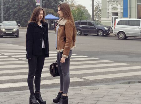 Two girls trying to cross the road at a pedestrian crossing. They have long brown hair and slender figures.の写真素材
