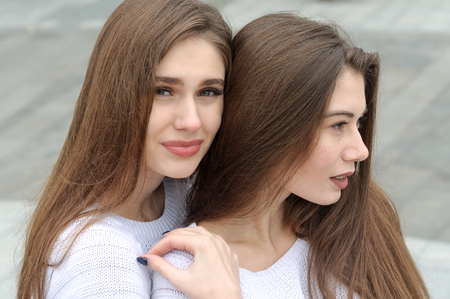 Close-up portrait of two close friends. They both have long brown hair that is long to the waist and they are dressed in identical white sweaters.の写真素材