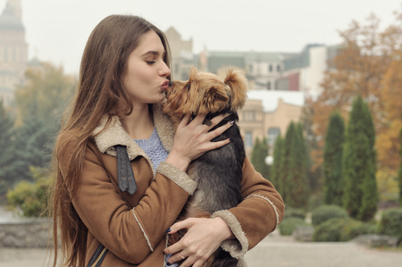 Girl holds a small dog in her arms, hugs and kisses her, warming her from the autumn cold.の写真素材