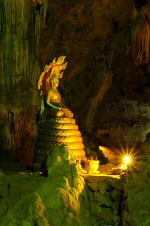 Golden Buddha image is placed peacefully in a dark cave with the candle light.の写真素材