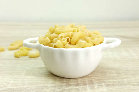 Dried pasta in a white bowl on the wood table.の写真素材