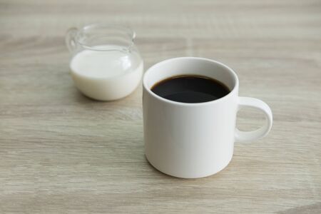 White coffee cup with transparent milk jar on the wood table.の写真素材