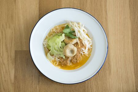 Coconut fish curry with rice noodle served with white enamel plate. Popular thai street food. 