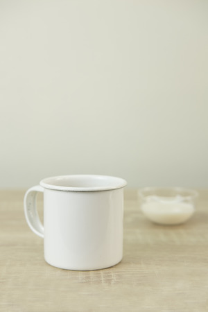 Enamel white coffee mug and small transparent milk bowl on a wood table.の写真素材