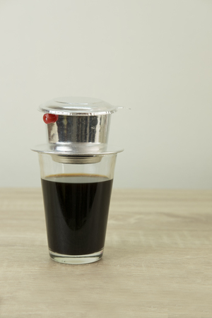 Coffee glass with black coffee and drip filter on a wood table.の写真素材