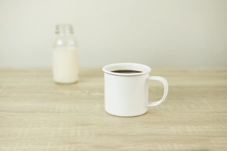 Enamel white coffee cup with milk bottle on a wood table.の写真素材