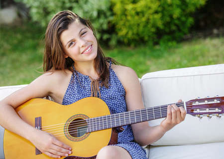 Portrait of very handsome teenager playing guitar in her garden