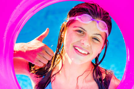 pretty girl smiling girl in a swimming pool looking in a pink buoy with the thumb up