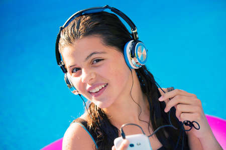smiling young girl listening to music in a pool with headphones