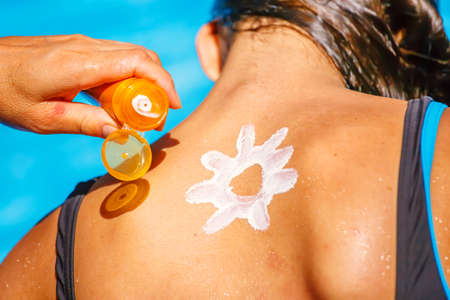 A mum applying a protect sun cream on the back of her young girl and drawing a funny sun