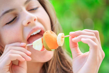 Lovely teenager with colorful clothes eating fresh fruits in a garden