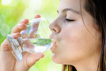 closeup of a healthy young girl drinking glass of water outdoorsの写真素材