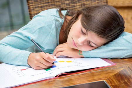 Tired or despondent young girl do homework lying on a table