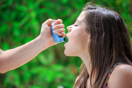 Portrait of a girl using inhaler for asthma from his mothers handの写真素材