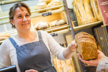 smiling woman with an apron selling bread in a bakery