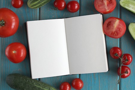 Note book and composition of vegetables on blue wooden desk. Tomato, cucumber. Top view.の写真素材