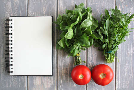 Note book and composition of vegetables on grey wooden desk. Tomato, basil, arugula. Top view. Modern photography. The best for recipies.の写真素材