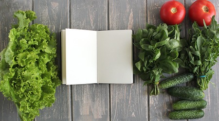 Note book and composition of vegetables on grey wooden desk. Tomato, basil, cucumber, arugula, lettuce. Top view. Modern photography. The best for recipies.の写真素材