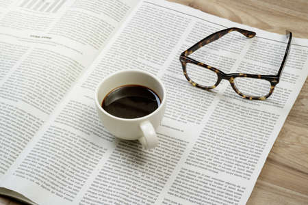 Newspaper on wooden table with coffee and eyeglasses.