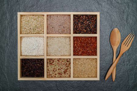 Top view nine kinds of rice.Brown rice, Black Jasmine rice, Red jasmine rice and Riceberry in boxes on black desk with fork and spoon.の写真素材