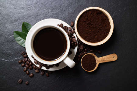 Top view mockup a cup of coffee with coffee beans and powder coffee in bowl on the black stone.