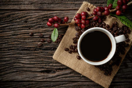 A cup of coffee on wooden desk with red ripe coffee beans.の写真素材