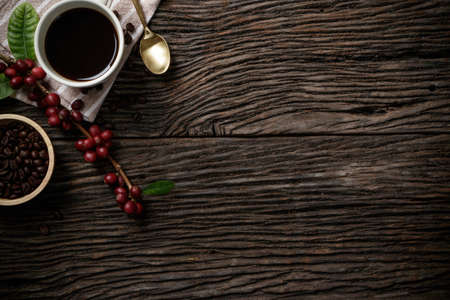Top view mockup on wood background with a cup of coffee and red ripe coffee beans. Top view with...