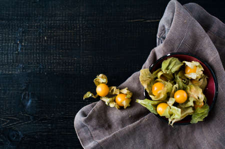Berries physalis in a black bowl, dark fabric, dark background, top view, space for text