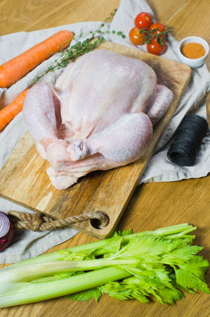 Raw chicken on a wooden chopping Board. Vegetables: carrots, onions, celery, tomatoes. Dark background, side viewの写真素材
