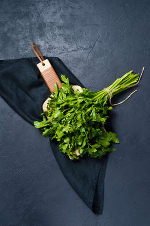 Bunch of parsley on a wooden chopping Board. Dark background, top view, space for textの写真素材