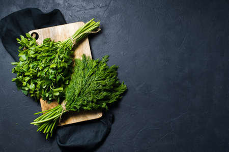 Dill and parsley on a wooden chopping Board. Dark background, top view, space for text