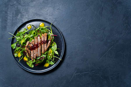 Salad with beef steak, arugula and chard on a black plate. Side view, black background, space for textの写真素材
