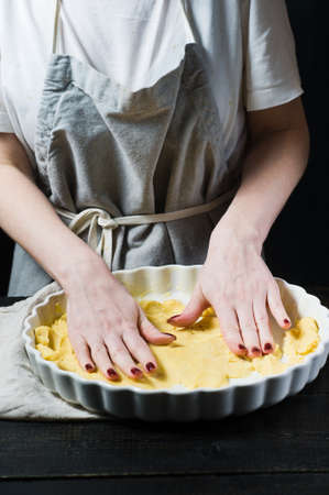 Chef rolls out the dough in a baking dish, cooking. Side view, black background, close up