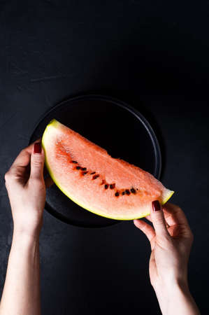 Hands holding a slice of watermelon. Dark background, top view
