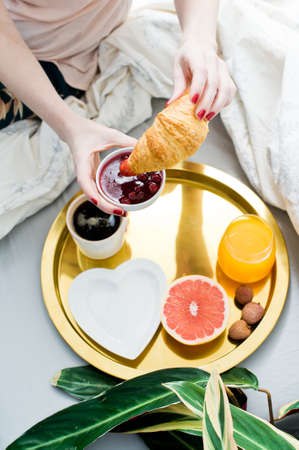 Girl eating croissant at Breakfast in the room, hotel service. Coffee, jam, croissant, orange juice, grapefruit, lychee. Side view, light background, close upの写真素材
