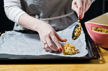 The chef is preparing cookies, spread the dough on the trays. Side view, black background, kitchen.