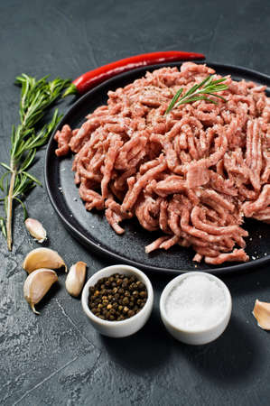 Raw ground beef on a stone Board. Ingredients for cooking, rosemary, chili pepper, garlic, salt. Black background, top viewの写真素材