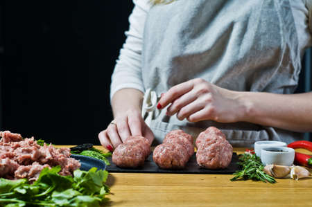 A female chef prepares Swedish meatballs from raw minced meat. Black background, side view, kitchenの写真素材