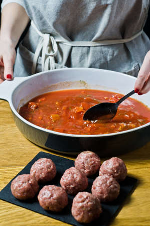 Chef prepares Swedish meatballs from raw minced meat, stir tomato sauce. Black background, top view, kitchenの写真素材