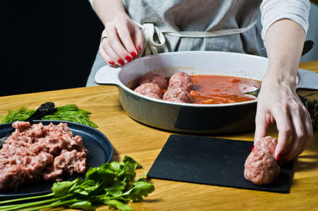 The chef prepares Italian meatballs from raw minced meat, puts in a baking dish with tomato sauce. Black background, top view, kitchenの写真素材